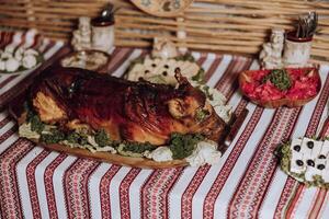 A large roast pig is on a wooden platter on a table with other food items. The tablecloth is red and white striped photo