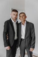 Two men in suits are standing next to each other. One of them is wearing a tie. Scene is formal and professional photo
