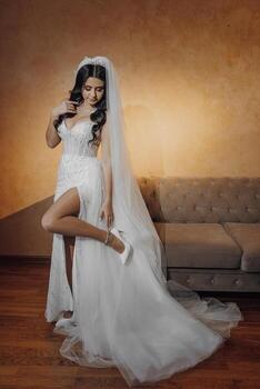 A woman in a white dress is posing for a picture. She is wearing a veil and has her feet up on a couch. The image has a romantic and elegant mood photo