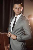 A man in a suit and tie is standing in front of a curtain. He is wearing a watch and he is adjusting his tie. Concept of formality and professionalism, as the man is dressed in a suit photo