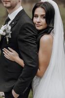 A bride and groom are posing for a picture. The bride is wearing a white dress and the groom is wearing a black suit. They are both smiling and looking at the camera. Concept of happiness and love photo