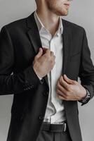 A man in a black suit and white shirt is adjusting his jacket. Concept of formality and professionalism, as the man is dressed in a suit and tie photo
