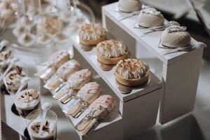 A table full of desserts including cakes, tarts, and other sweet treats. The desserts are arranged on a white table and are presented in small cups. The table is decorated with a variety of desserts photo
