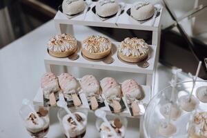 A dessert table with a variety of desserts including cupcakes, cookies, and ice cream. The desserts are arranged on a white table and are presented in clear plastic cups photo