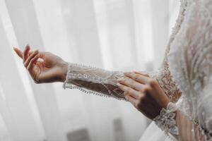 A woman is wearing a white dress and is holding her arm up to show off her sleeve. The dress is long and has a lace-like design. The woman's hand is holding a button, which is likely part of the dress photo