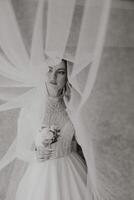 A woman in a wedding dress is holding a bouquet of flowers. The image has a romantic and elegant mood photo