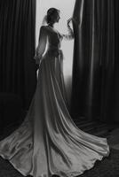 A woman in a wedding dress stands in front of a curtain. The dress is long and flowing, and the woman is wearing a veil. The image has a moody and dramatic feel photo