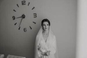 A woman in a wedding dress stands in front of a clock with the hands on the numbers 9 and 3 photo