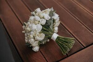 A bouquet of white flowers sits on a wooden table. The flowers are arranged in a way that they are all facing the same direction, creating a sense of unity and harmony photo