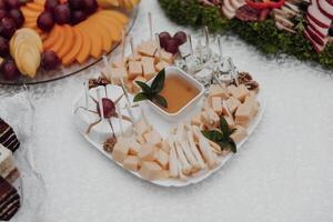 A white plate with a variety of cheeses and fruit on it. The plate is placed on a table photo