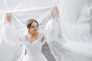 A woman in a white dress is standing in front of a white curtain photo