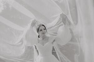 A woman in a white dress is standing in front of a white sheet, with her arms spread out photo
