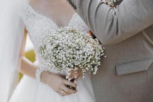 A bride and groom are holding hands and the bride is holding a bouquet of white flowers. Scene is romantic and happy photo