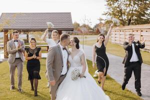 A bride and groom are surrounded by their wedding party, all dressed in black and white. The bride is wearing a white dress and the groom is wearing a suit. The wedding party is all smiling photo