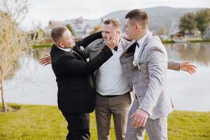 Three men are playing around in a grassy area near a body of water. One of the men is wearing a suit and tie photo