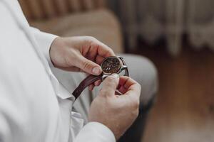 A man is wearing a watch and adjusting it. The watch is brown and has a silver band photo