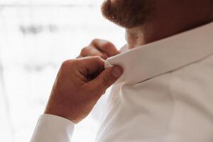 A man is getting dressed and adjusting his collar photo