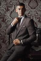 A man in a suit is sitting at a table and adjusting his tie photo