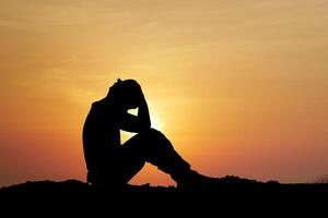 Silhouette of a Person Sitting at Sunset with Hands on Head, Contemplating and Reflecting in a Tranquil Outdoor Setting photo