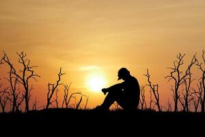 Silhouette of a Person Sitting Alone at Sunset with Bare Trees in the Background photo