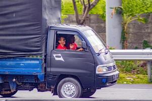 The man driving the Suzuki Carry pick-up car was relaxed and joking with the passenger beside him, Indonesia, 16 July 2024. photo