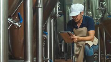 Asian male worker with tablet examining beer quality at craft brewery factory. photo