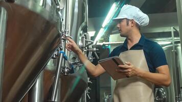 Asian male worker with tablet examining beer quality at craft brewery factory. photo