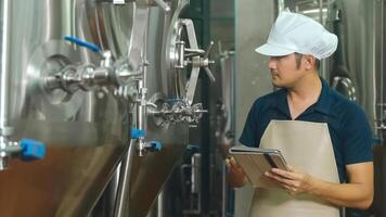 Asian male worker with tablet examining beer quality at craft brewery factory. photo