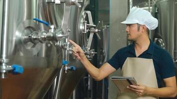Asian male owner with tablet examining beer quality at craft brewery factory. photo