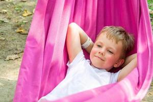 A beautiful boy lies in a pink hammock on a background of blurred greenery photo