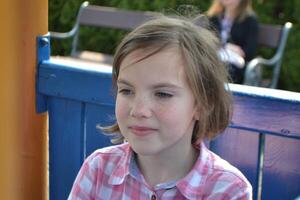 The girl sits on a bench in park. There is a flower ornament on her head photo
