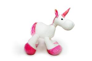 Pink soft unicorn toy sitting at white background. Isolated studio image photo