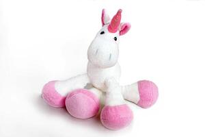 Pink soft unicorn toy sitting at white background. Isolated studio image photo
