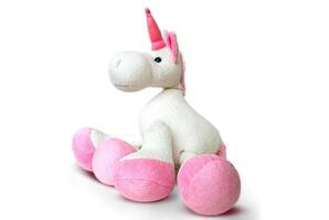 Pink soft unicorn toy sitting at white background. Isolated studio image photo