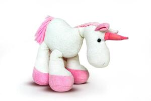 Pink soft unicorn toy sitting at white background. Isolated studio image photo