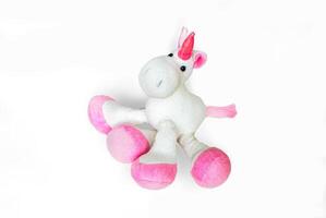 Pink soft unicorn toy sitting at white background. Isolated studio image photo