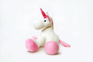 Pink soft unicorn toy sitting at white background. Isolated studio image photo