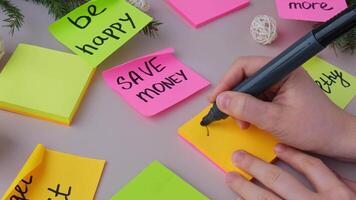 LOVE MORE text Unrecognizable woman writing new year's resolutions on colorful sticky notes. Making promises for new year, setting goals. Creating vision board motivation video