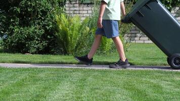 boy rolls out trash can. Boy throws out garbage. Child helps with chores video