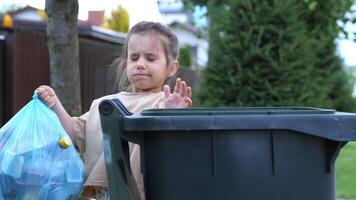 close-up A little girl throws a full trash bag of garbage into a trash can. video