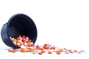 Colorful pills spilling out of black plastic container isolated on white background photo