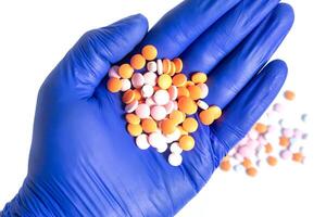 Hand in blue glove holding a pile of multicolor pills isolated on white background. closeup photo
