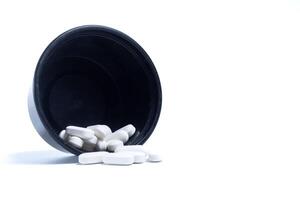 pills spilling out of a black plastic container leaning against a white background. Closeup photo