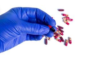 Hand in blue glove holding red and black capsules isolated on white background. Top view photo