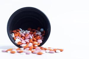 Multicolor pills spilling out of spilled from black plastic box on white background. closeup photo