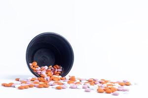 Multicolor pills spilling out of spilled from black plastic box on white background. closeup photo