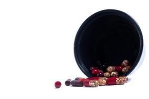 Pills spilling out of a black plastic container isolated on white background photo