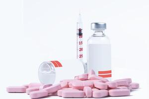 Vaccine bottle and syringe with pink pills on white background photo