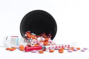 Vaccine bottle with spilled multicolored pills and syringe on side on white background. photo