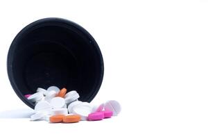 Pills spilling out of a black plastic container leaning against a white background. Medical health care concept. photo